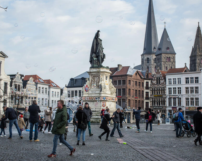 Vrijdagsmarkt met middeleeuwse gebouwen, op de achtergrond de Sint-Jacobskerk. In het midden van de Vrijdagsmarkt staat het standbeeld van Jacob Van Artevelde. Er wandelen verschillende mensen over de markt.