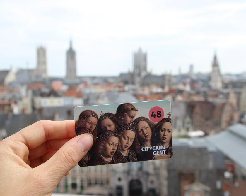 Hand mit City Card Gent (18 Std.) mit im Hintergrund die bekannte Skyline von Gent. (Vom Dach des Grafenburgs)