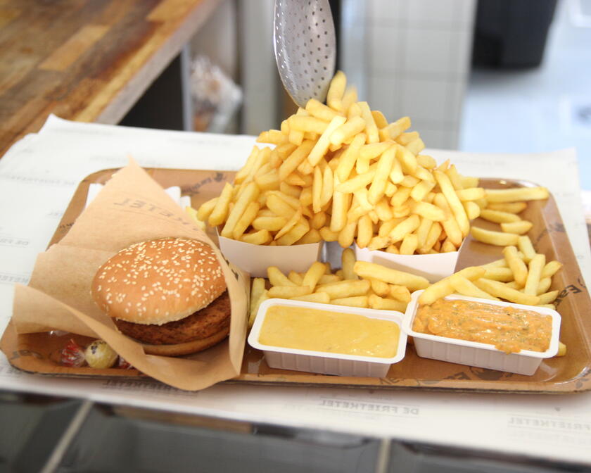 Dienblad met hamburger in papieren omslag, 2 zeer grote porties friet en 2 sausjes.