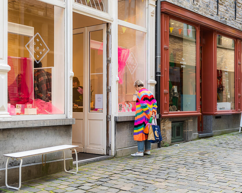 Une femme avec un pull à rayures colorées regarde dans la vitrine d’un magasin de la Serpentstraat à Gand