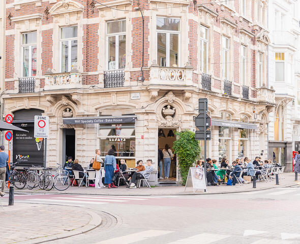 Menschen sitzen auf einer Terrasse in der Einkaufsstraße von Gent