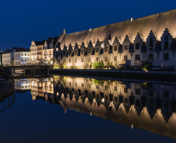 De verlichte middeleeuwse gevel van het Groot Vleeshuis langs het water in Gent 