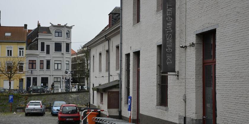 Voorgevel van de Geus van Gent. Witte, bakstenen voorgevel met fietsenstalling. Op de achtergrond zie je de huizen van de Muinkkaai.
