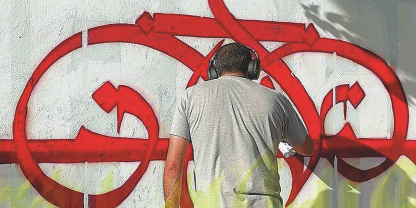 een man die rode graffiti op een muur aan het spuiten is en een koptelefoon draagt