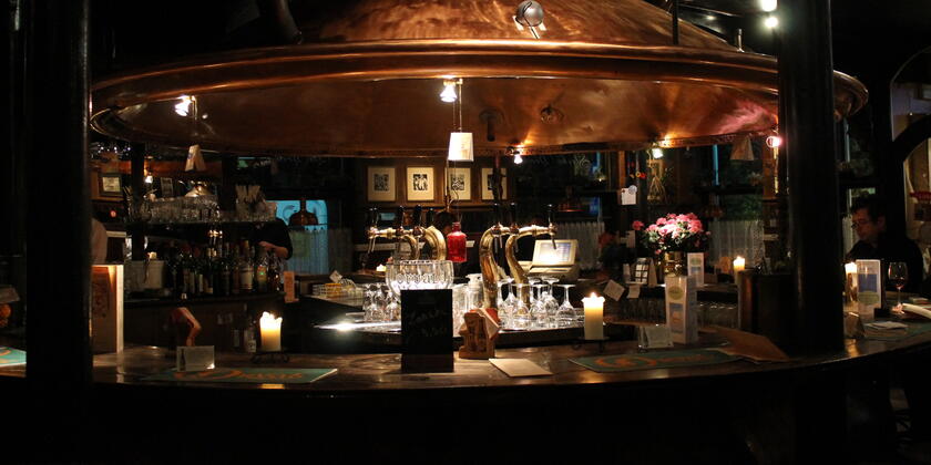 Ronde toog van café De Brouwzaele onder het roodkoperen deksel van een bierketel.
