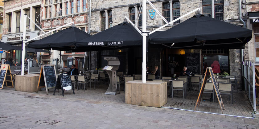 Gevel van restaurant Borluut, in Doornikse breuksteen, terras onder grote zwarte parasols.