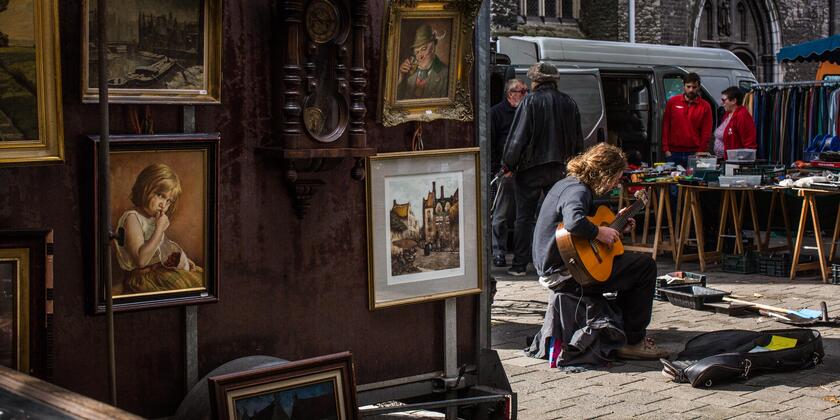Gitarist op de Brocantemarkt bij Sint-Jacobs, kraam met schilderijen op de voorgrond.