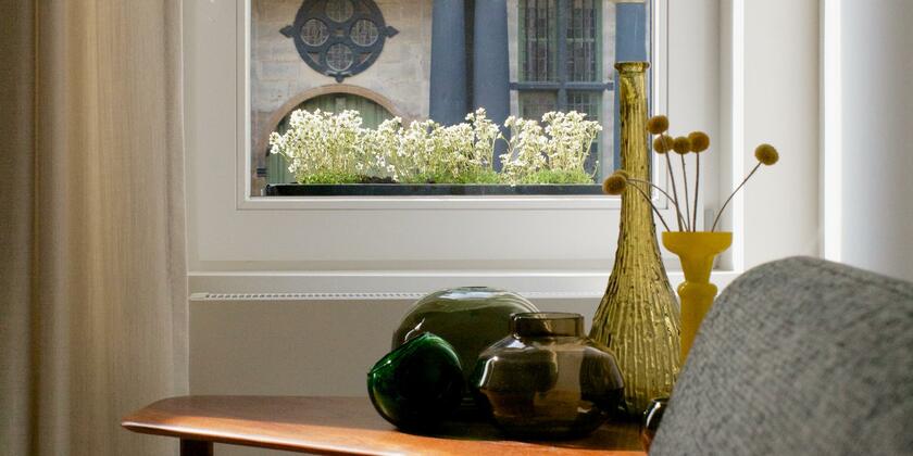 grijze zetel naast een tafel met vazen, raam met uitzicht gebouw met blauwe zuilen met een gouden rand, bloemen in plantenbakken