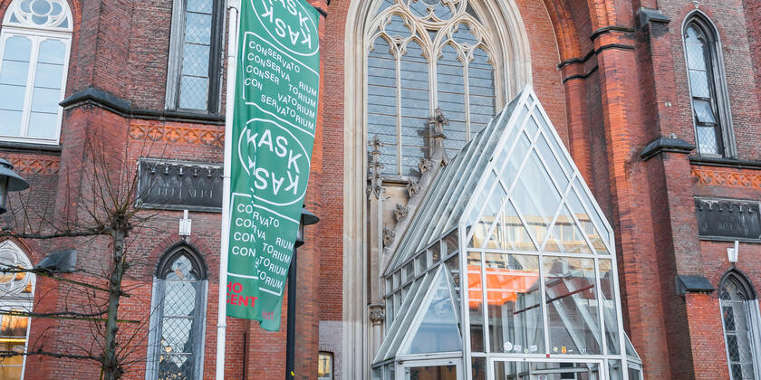 Vordereingang KASK, Glasaufbau vor dem Eingang, grüne Fahne mit KASK darauf, Fahrräder 