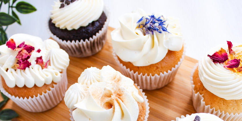 6 cupcakes met witte crème en bloemen op een houte plank