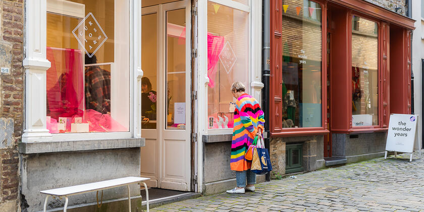Vrouw met kleurrijke streepjestrui kijkt in etalage van winkel in de Serpentstraat in Gent
