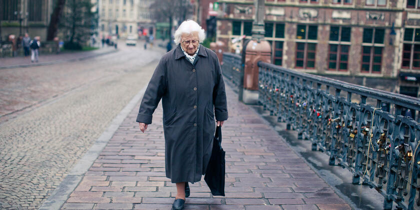 Oude dame stapt over de Sint-Michielsbrug op druilerige dag
