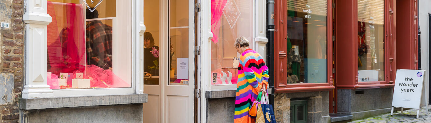 Frau mit bunt gestreiftem Pullover schaut in das Schaufenster eines Geschäfts in der Serpentstraat in Gent