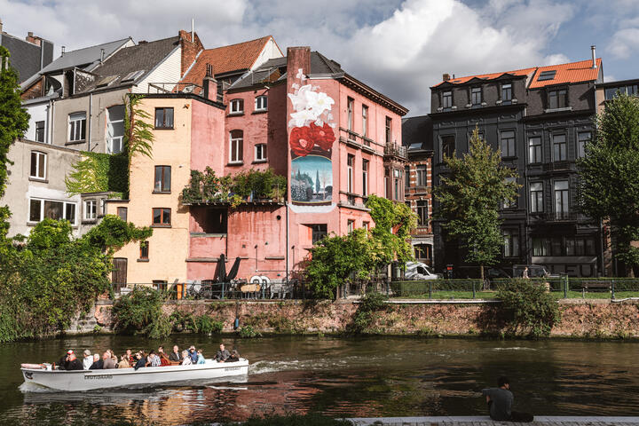 een boot met mensen op het water, een gebouw met street art naast andere gebouwen