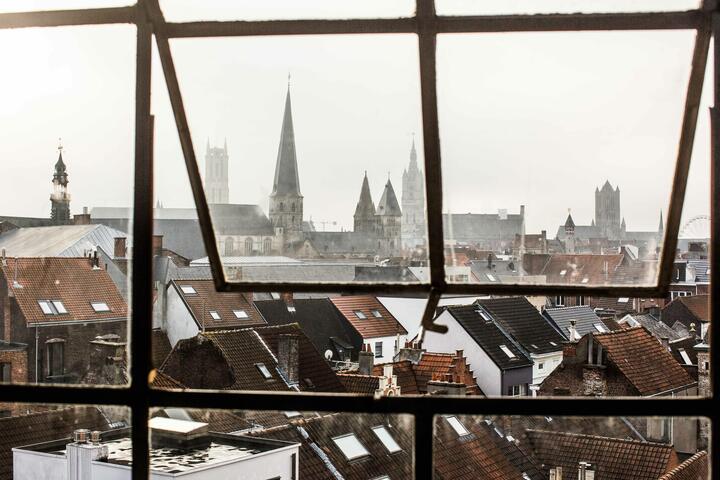 een raam dat openstaat en dat uitkijkt over de daken van Gent