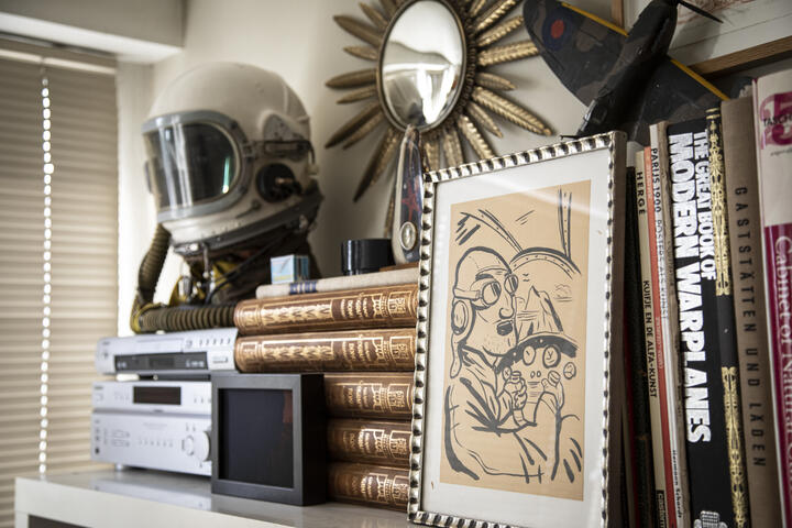een plank met daarop verschillende boeken, een astronautenhelm, een spiegel, een tekening