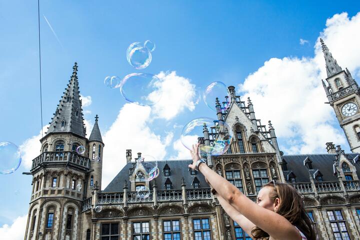 Vrouw die zeepbellen probeert te vangen voor  het voormalige neogotische postgebouw.