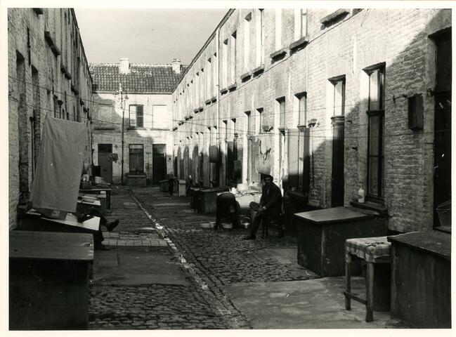 Black and white photo of resident sitting on chair in a Ghent alley