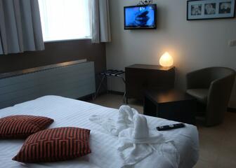 Hotelkamer, bed met kussens, handdoek en afstandsbediening, tv-scherm.