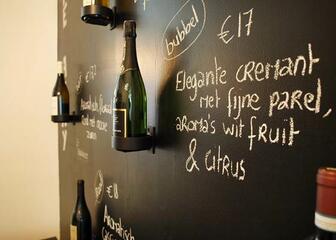 Close-up van wijnflessen aan de muur met opschriften ernaast.