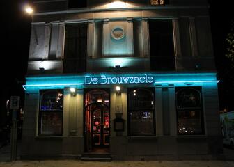 Buitenzicht van café De Brouwzaele, met lichtblauwe neon balk als blikvanger.