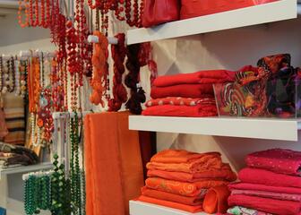 Detail binnen in de winkel: sjaals en juwelen in rode tinten.