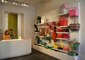 Foto binnen in de winkel: kassa, twee verkoopsters, verkoopartikelen in felle kleuren.