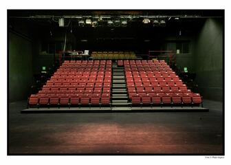 Binnenzicht van theater Minnemeers met rijen rode zitjes en een groot podium.