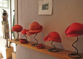 Verschillende hoeden in verschillende tinten rood op metalen staanders.