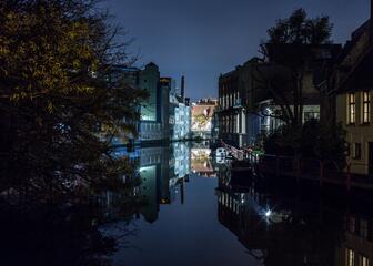 Gante de noche, vista sobre el río, edificios iluminados reflejados en el agua.