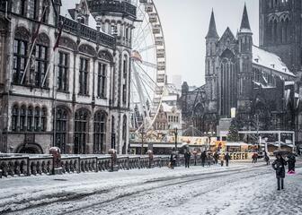 Zicht vanop de Sint-Michielsbrug met Postgebouw, reuzenrad en Sint-Niklaaskerk in de sneeuw.