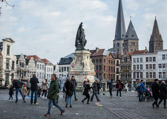 Vrijdagsmarkt met middeleeuwse gebouwen, op de achtergrond de Sint-Jacobskerk. In het midden van de Vrijdagsmarkt staat het standbeeld van Jacob Van Artevelde. Er wandelen verschillende mensen over de markt.