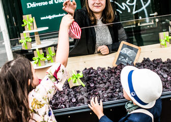 Verkoopster geeft een rood/wit gestreept zakje cuberdons aan twee kindjes aan het kraampje op de Groentenmarkt in Gent