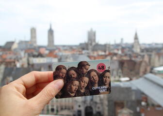 Hand holding citycard Ghent (48h) with in the background the well-known skyline of Ghent (Taken from the top of the Castle of Counts)