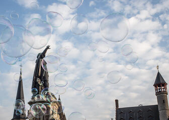 Foto van Jacob Van Artevelde en 't Toreken op de Vrijdagsmarkt. Op de achtergrond een lichtbewolkte, blauwe lucht en alles is omgeven met zeepbellen.