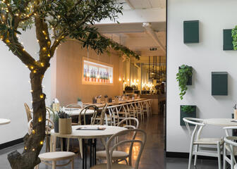 Interieur van restaurant Gust met planten aan de muur en een verlichte boom in de zaal.