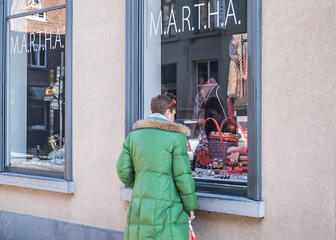 Vrouw met felgroene winterjas bekijkt etalage van Marthe. 
