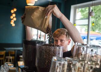 Een barista giet koffiebonen in de koffiemolen.