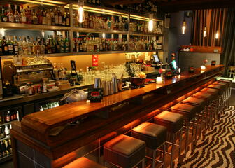 De bar van café Zoo met hoge barstoelen voor de lange houten toog en een groot assortiment sterke drank en mixers.