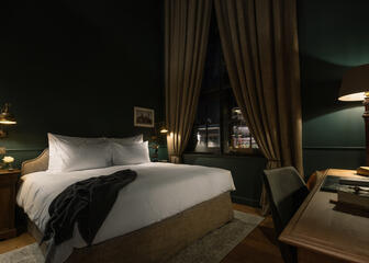 Donkere, stijlvol ingerichte hotelkamer, tweepersoonsbed en schrijftafel.