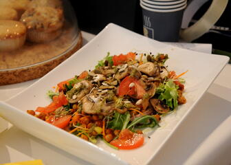 wit bord met slaatje van sla, tomaat, kikkererwten, wortels, champignons, stolp met cupcakes onder