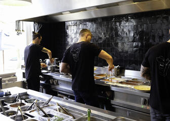 Drie koks met zwart t-shirt aan het werk in de keuken van een restaurant.