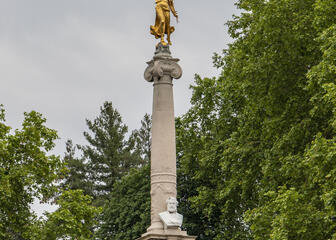 monument met gouden beeldje vanboven, voor bomen