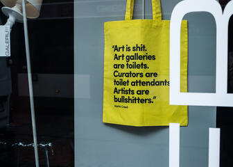 Detail van een gele tote bag met quote die in de etalage hangt.