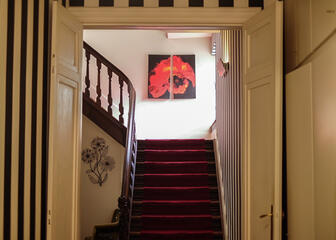 Traphal met rood tapijt op de trap, aan de muur hangt een foto van een klaproos.