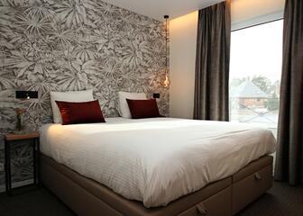 Tweepersoonskamer met klein terras. Bed staat tegen de muur met floraal behangpapier.