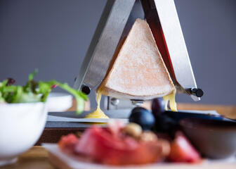 close-up raclette met ervoor een kom sla en een bord tomaten 