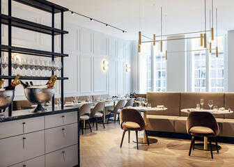 Restaurant met hoge plafonds, vierkante en ronde tafels, banken en kuipstoelen.