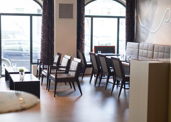 Ruimte met bruine tafels en stoelen, gordijnen met een lijnpatroon. 