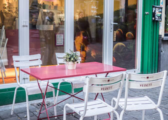 Eenvoudig terras met roze tafels en witte stoelen.